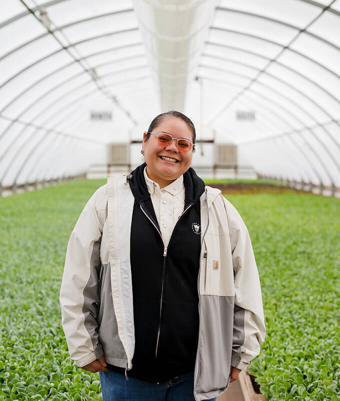 a person standing in a greenhouse with asparagus smiling.
